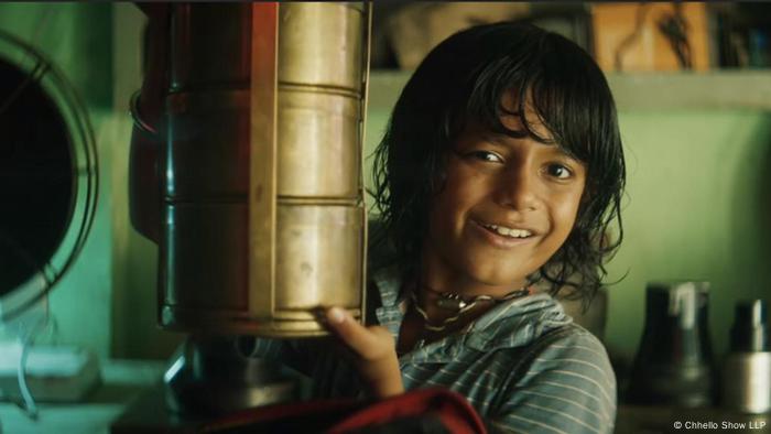 Ein Junge mit halblangen Haaren steht lächelnd neben einem Filmprojektor