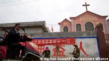 In this photo taken Saturday, June 2, 2018, a man rides past workers tossing hay outside a church with part of a slogan that reads Educate the believers with excellent Chinese traditional culture near the city of Pingdingshan in central China's Henan province. Under President Xi Jinping, China's most powerful leader since Mao Zedong, believers are seeing their freedoms shrink dramatically even as the country undergoes a religious revival. Experts and activists say that as he consolidates his power, Xi is waging the most severe systematic suppression of Christianity in the country since religious freedom was written into the Chinese constitution in 1982. (AP Photo/Ng Han Guan)