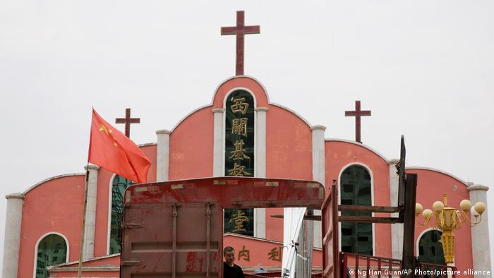 A worker looks out from a truck parked in front of a church and the Chinese national flag