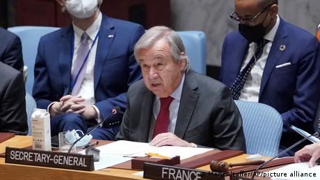 António Guterres sitzt an einem Pult mit Mikrofon. Vor ihm befindet sich ein Schild mit der Bezeichnung SECRETARY-GENERAL, hinter ihm sitzen zwei Männer. (Quelle: Mary Altaffer/AP/picture alliance)