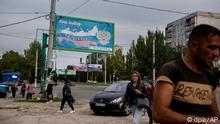 22.09.2022, Ukraine, Luhansk: Menschen gehen in der von Russland unterstützten und von Separatisten kontrollierten Volksrepublik Luhansk in der Ostukraine an einem Plakat mit der Aufschrift «Unsere Wahl - Russland» vorbei. Die Behörden in den russisch-kontrollierten Regionen in der Ost- und Südukraine bereiten sich auf Scheinreferenden über die Zugehörigkeit zu Russland vor - ein Schritt, der es Moskau ermöglichen könnte, den Krieg eskalieren zu lassen. Die Abstimmungen beginnen am Freitag, 23.09.2022 in den Regionen Luhansk, Cherson und den teilweise russisch kontrollierten Regionen Saporischschja und Donezk. Foto: Uncredited/AP/dpa +++ dpa-Bildfunk +++