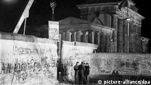 Das Archivbild vom 22.12.1989 zeigt Polizeibeamte aus Ost- und West-Berlin, die sich an der geöffneten Mauer am Brandenburger Tor unterhalten, während hinter ihnen mit einem Kran ein Stück Mauer in die Höhe gehoben wird. Nach der Öffnung eines Teils der deutsch-deutschen Grenzübergänge in der Nacht vom 9. auf den 10. November 1989 reisten Millionen DDR-Bürger für einen kurzen Besuch in den Westen. In der Folge wurde die innerdeutsche Grenze abgebaut, seit dem 3. Oktober 1990 ist Deutschland wieder vereint. dpa (zu dpa-Themenpaket: Zehn Jahre Wende/Mauerfall vom 01.11.1999) +++ dpa-Bildfunk +++