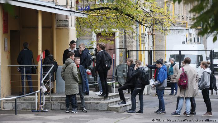 Zdjęcie przedstawia kolejkę mężczyzn czekających na wejście do budynku.