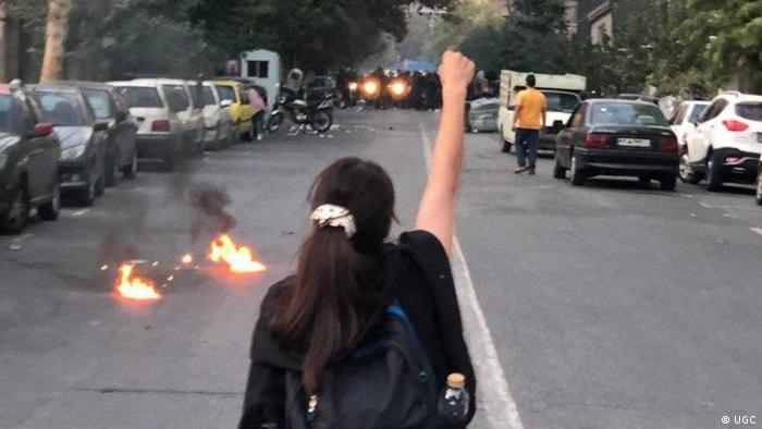 A woman holds up a defiant arm as fires burn on the street
