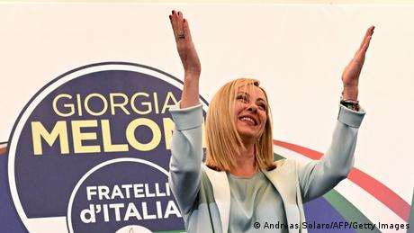 Georgie Meloni hebt vor einem Wahlplakat dankend die Hände in Richtung eines nicht sichtbaren Publikums