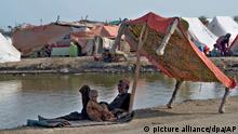 Im Schatten eines aufgestellten Bettes sitzt ein Mann am Straßenrand. In Pakistan haben Behörden ihre Bürger zur Unterstützung der Flutopfer im Land aufgerufen. Der Regierung fehle es an Kapazitäten, um das Ausmaß der katastrophalen Flut zu bewältigen, hieß es am Dienstag. (zu dpa Pakistan ruft eigene Bürger zur Hilfe von Flutopfern auf +++ dpa-Bildfunk +++