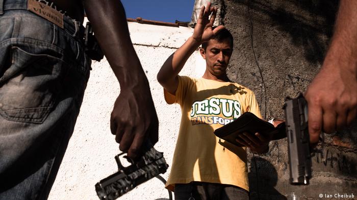 Un hombre con una camiseta en la que dice Jesús transforma predica ante hombres armados.