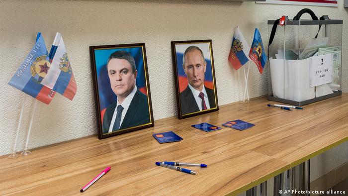 Fotos vom selbsternannten Führer der Voksrepublik Luhansk, Leonid Pasechnik, und Putin stehen neben einer Box mit Stimmzetteln.