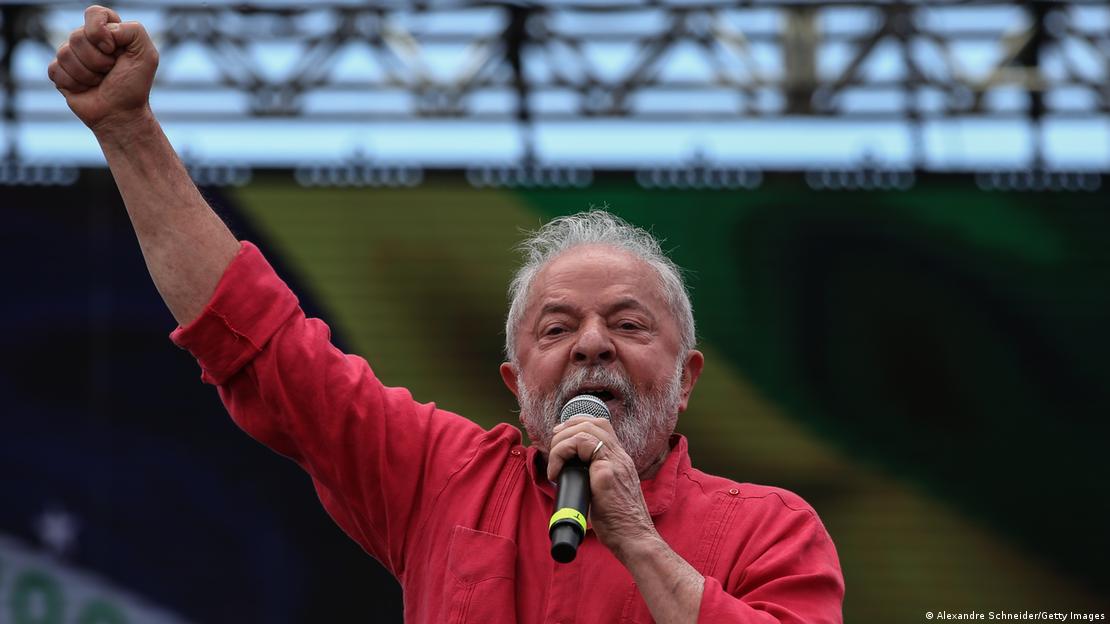 Lula de camisa vermelha discursa em frente a painel com a bandeira do Brasil