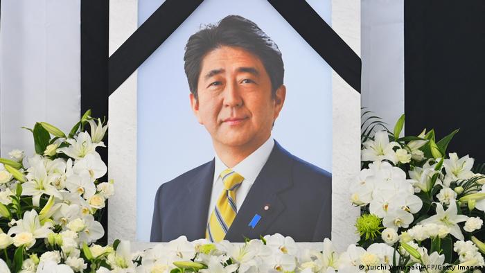 An image of former Japanese prime minister Shinzo Abe is displayed at the stands set up outside the Nippon Budokan in Tokyo on September 27, 2022, as people queue up to leave flowers ahead of his state funeral. 