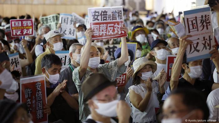 Demonstrators hold signs during a protest against the planned state funeral for slain former Japanese Prime Minister Shinzo Abe in front of Tokyo's JR Shinjuku Station on Sept. 26, 2022, the eve of the ceremony.