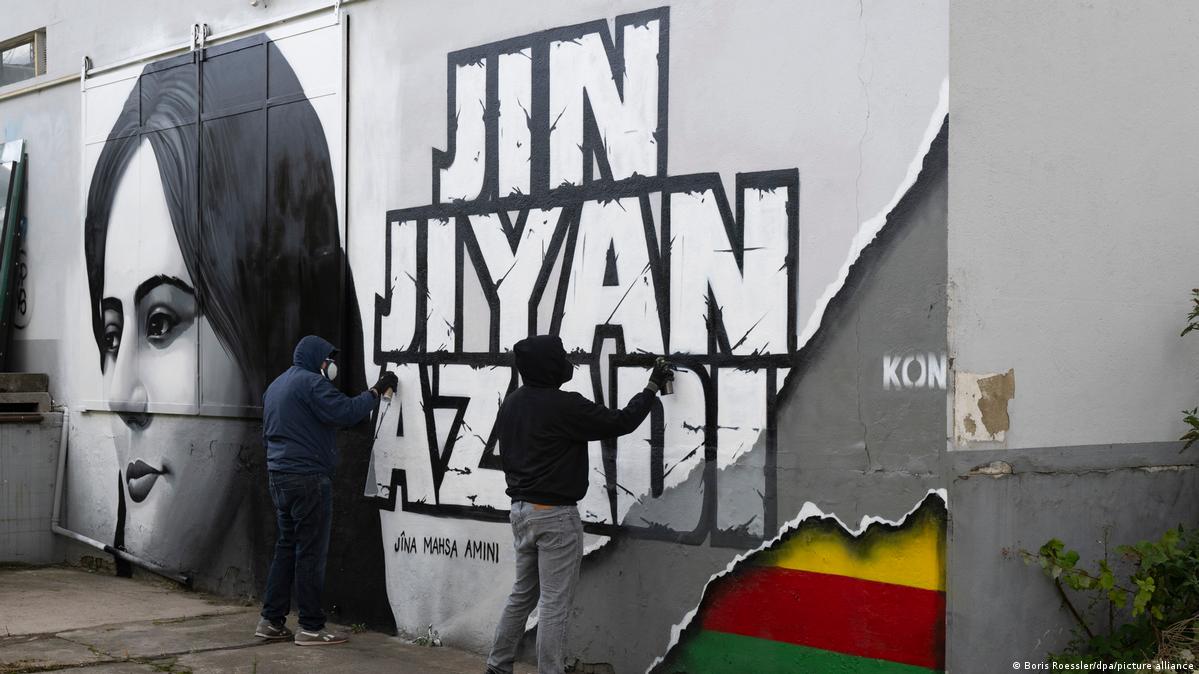 Palavras em farsi Jin, Jiyan, Azadi (mulheres, vida, liberdade) pintadas numa parede em Frankfurt ao lado do retrato de Mahsa Amini