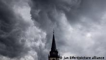 Dunkle Wolken eines Schauers sind am Abend am Himmel über dem Kirchturm der katholischen Kirche St.-Ursula in Oberursel zu sehen.