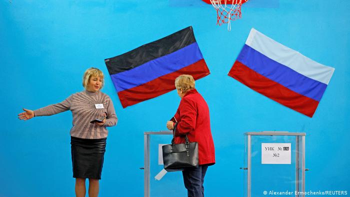 Una organizadora indica el camino a una votante tras emitir su voto bajo las banderas de Rusia y de la autoproclamada república de Donetsk.