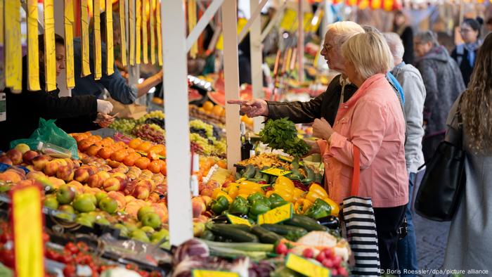 Dos clientes preguntan en un puesto de fruta.