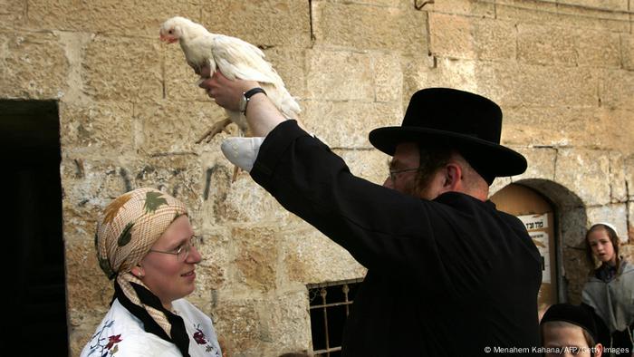 Ein orthodoxer Jude hält ein Huhn über den Kopf einer Frau. 