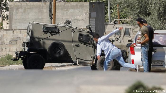 Palestinos lanzan piedras contra un vehículo militar israelí.