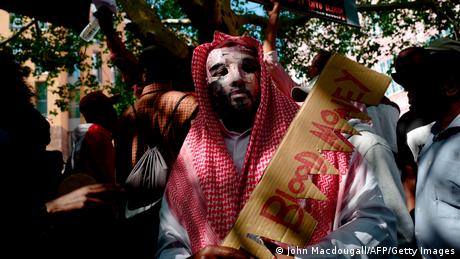 An activist dressed in traditional Saudi garb holds a cardboard saw with blood money at a protest in Berlin. 