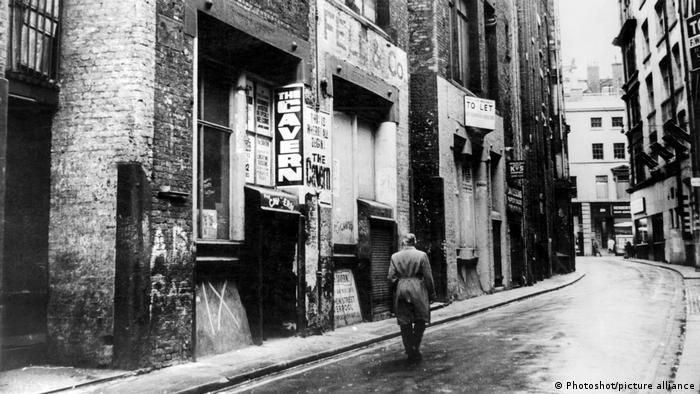 black and white photo of a person walking down a road with signs at entrance of The Cavern Club.