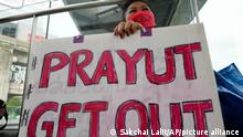 A anti-government protester holds a sign reading 'prayut get out'