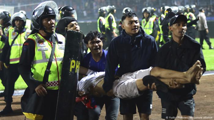Soccer fans carry an injured man following clashes during a soccer match at Kanjuruhan Stadium in Malang