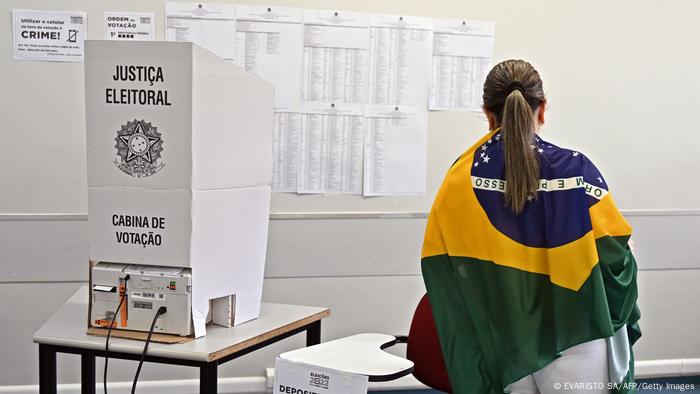 Una mujer vota con una bandera de Brasil sobre su espalda.