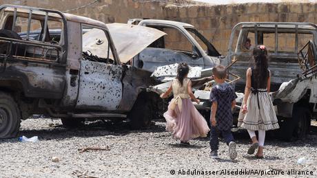Damaged vehicles and Yemeni kids run after an attack by the Iranian-backed Houthis in Taiz
