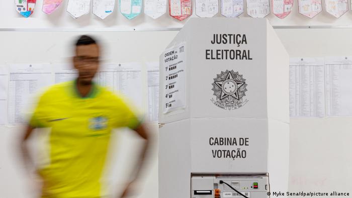 Un hombre con una camiseta en los colores de Brasil, frente a una cabina electoral.