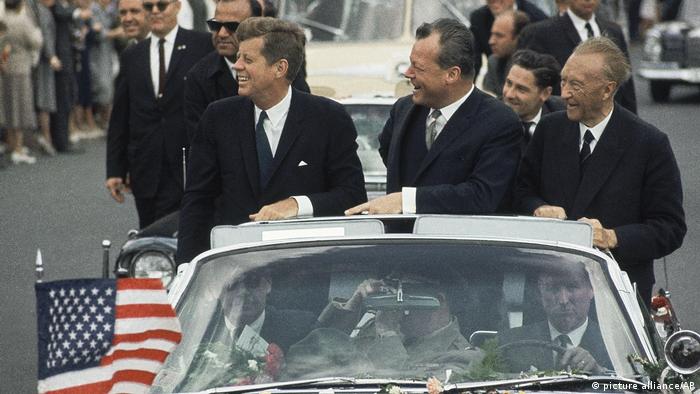 US-Präsident John F. Kennedy, der Regierende Bürgermeister von West-Berlin, Willy Brandt, und Bundeskanzler Konrad Adenauer fahren stehend in einer amerikanischen Staatskarosse durch Berlin