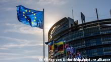 EU Parliament building with EU and member state flags under a sunny evening sky in Strasbourg, France