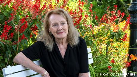 French writer Annie Ernaux sitting on a bench in front of flowers.
