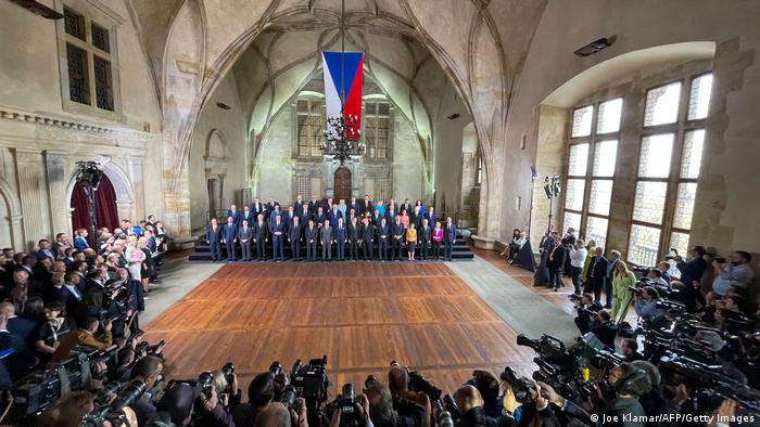 Gruppenbild: Die Politiker stehen aufgereiht in einer gotischen Halle gegenüber Gästen und Pressevertretern mit Kameras.