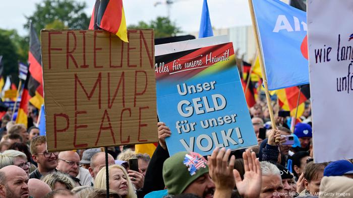 AfD-Demonstranten halten bunte Plakate mit unterschiedlichen Parolen in die Höhe; auf einem Schild steht Frieden, auf einem anderen Alles für unsere Heimat 