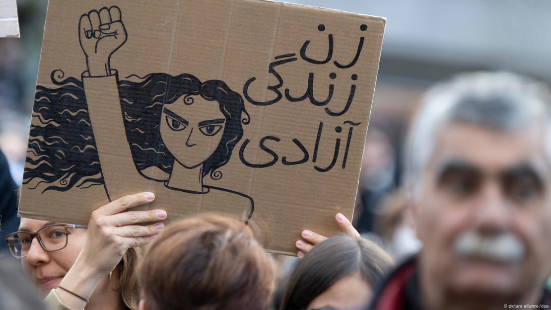 Mulher empunha cartaz mostrando desenho de uma mulher com punho levantado e letras árabes