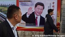 TOPSHOT - People walk past a poster featuring Chinese President Xi Jinping with a slogan reading Chinese Dream, People's Dream beside a road in Beijing on October 16, 2017. As Chinese leader Xi Jinping prepares to embark on a second five-year term this week, the impulsive leaders of North Korea and the United States could spoil his party. / AFP PHOTO / GREG BAKER (Photo credit should read GREG BAKER/AFP via Getty Images)