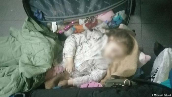 Child curled up sleeping in a suitcase at the Kunichino Gora checkpoint in Russia on the border with Estonia