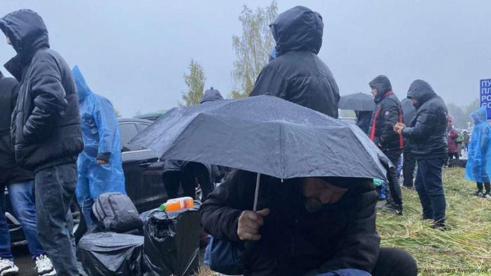 Ukrainian refugees waiting in line at the Kunichino Gora checkpoint in Russia at the border with Estonia, wearing raincoats and holding umbrellas