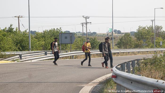 Flucht in Europa. Das Foto zeigt vier junge Männer aus Pakistan, die eine leere Straße in Griechenland überqueren. Sie kommen aus der Türkei, tragen Rucksäcke und sind auf dem Weg zur Balkan-Route. 