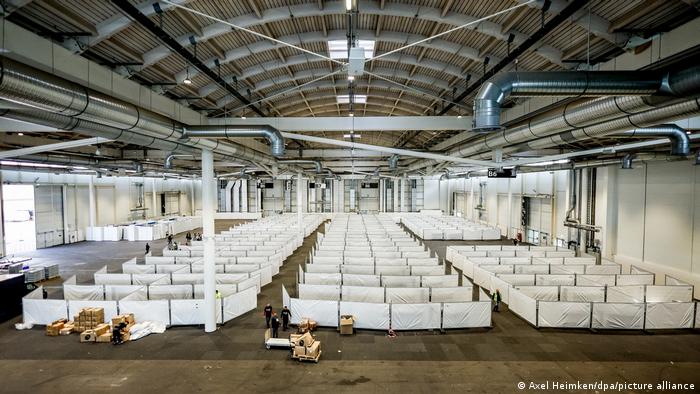 Flüchtlinge in Deutschland. Blick in eine Messehalle. Arbeiter bereiten die Halle für die Unterbringung von Schutzsuchenden aus der Ukraine vor. Die Halle soll kurzfristig mit rund 400 Menschen belegt werden. In drei Reihen werden mit weißen Planen Trennwände aufgestellt, um einzelne Parzellen zu markieren.