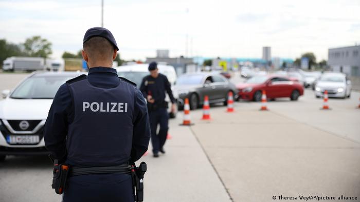 Österreich Kittsee | Grenze zur Slowakei. Ein österreichischer Grenzpolizist in dunkelblauer Uniform steht mit dem Rücken zur Kamera vor einer Schlange von Autos. Ein zweiter Grenzpolizist kontrolliert Pässe. 