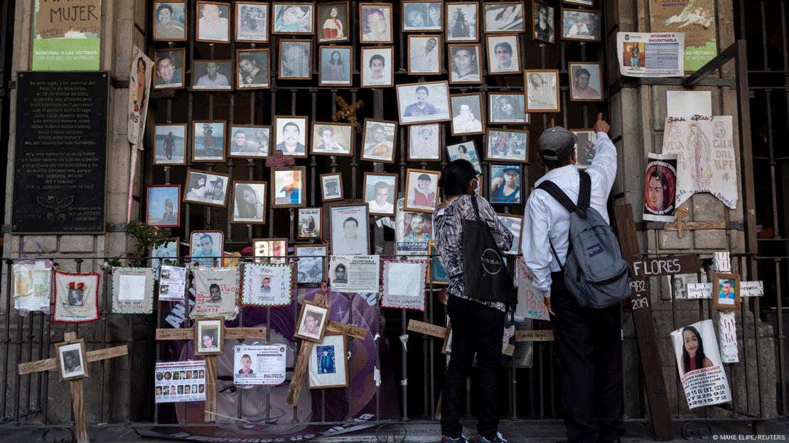 Una hombre y una mujer señalan retratos de personas desaparecidas por el accionar del crimen organizado en México.