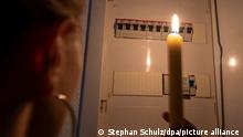 Eine Frau hält bei einem Stromausfall eine Kerze in der Hand und blickt in einen Sicherungskasten. || Modellfreigabe vorhanden