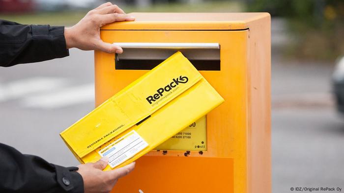 Un persona introduciendo un sobre de cartón reciclable en un buzón.