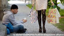 Mann sitzt auf einem Buergersteig und bettelt, junge reiche Frau mit Einkaufstaschen geht an ihm vorbei, Deutschland | unemployed beggars living on the street, rich young woman with shopping bags passing ihn, Germany
