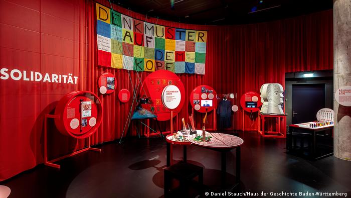 Verschiedene Ausstellungsstücke zum Thema Umdenken und Solidarität sind vor einem roten Vorhang platziert.