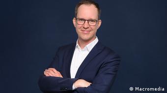 Florian Meißner is professor for media management and journalism at Macromedia, University of Applied Sciences in Cologne, Germany. He is wearing a dark suit with a white shirt, and his arms are crossed in a comfortable possition. He is wearing glasses and he is smiling. 
