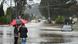 Two residents in Victoria stand on a street looking at a car partially submerged in flood water Two residents in Victoria stand on a street looking at a car partially submerged in flood water