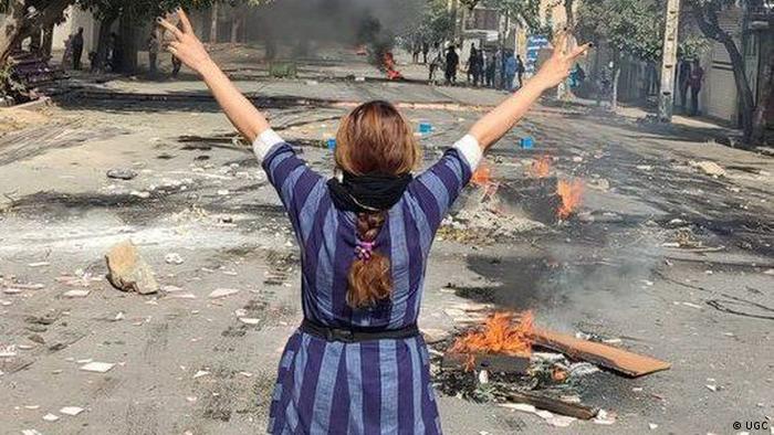 Imagen de una mujer de espaldas, con el cabello suelto y sin velo, en medio de una barricada incendiada en una calle de Teherán.