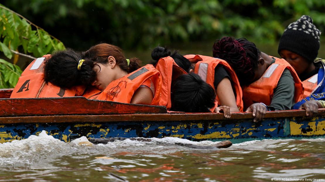 Pessoas de coletes salva-vidas laranja dormem sentadas em uma canoa