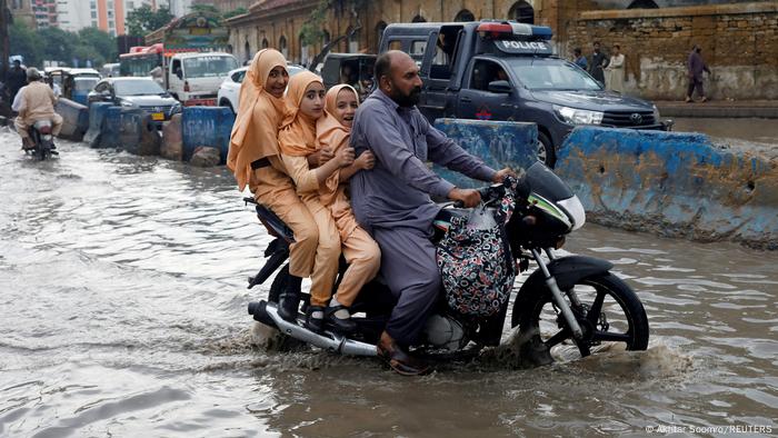 Mann fährt mit drei Mädchen auf dem Motorrad über überschwemmte Straße